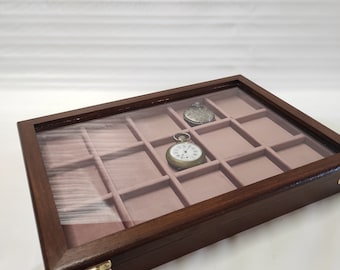 Op de afbeelding: Een donkerbruine houten doos met een glazen deksel en een fluwelen interieur. De doos heeft 12 vakken voor het opbergen van zakhorloges. Twee zakhorloges zijn zichtbaar in de doos.