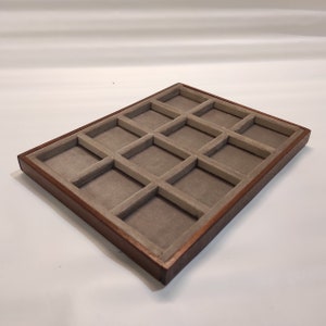 Può includere: Un vassoio in legno con 16 scomparti rivestiti in feltro grigio. Il vassoio è perfetto per organizzare ed esporre piccoli oggetti.