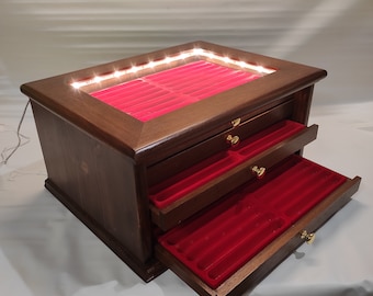 Könnte beinhalten: Eine Holzkästchen für Schmuck mit Glasdeckel und drei Schubladen. Die Box ist mit rotem Samt ausgekleidet und hat eine Innenbeleuchtung. Die Schubladen sind geöffnet und zeigen die rote Samtfütterung.