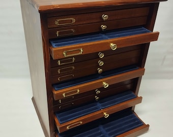 Op de afbeelding: Een houten kast met 12 lades, elk met een messingknop en een klein messing etiketthoudster. De lades zijn bekleed met blauw fluweel. De kast is gemaakt van donker hout en heeft een gepolijste afwerking.