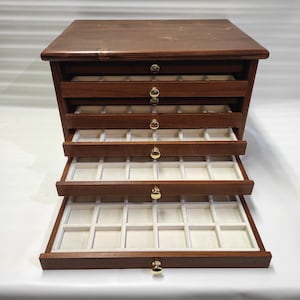May include: A wooden jewelry box with five drawers. The drawers are lined with white felt and have gold-colored knobs. The box is closed, but the top drawer is slightly open.