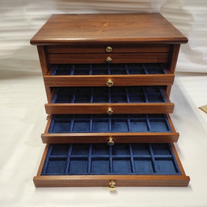 May include: A wooden jewelry box with five drawers. Each drawer is lined with blue velvet and has multiple compartments. The box has gold-colored knobs.