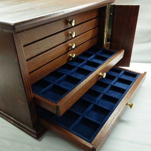 May include: A wooden jewelry box with a dark brown finish. The box has multiple drawers with gold-colored knobs and blue velvet-lined compartments. The top of the box is closed, and one side is open, revealing the interior.