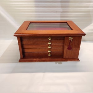 May include: A wooden display case with a glass top and six drawers. The drawers have gold knobs and the case has a keyhole with a red tassel.
