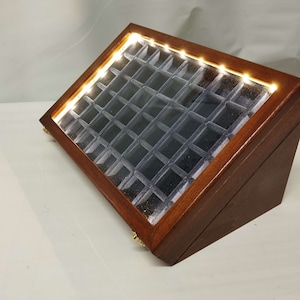 Könnte beinhalten: Eine Holzausstellungskiste mit einer Glasplatte und einem Licht im Inneren. Die Kiste hat mehrere Fächer zur Aufbewahrung von kleinen Gegenständen wie Schmuck oder Münzen.
