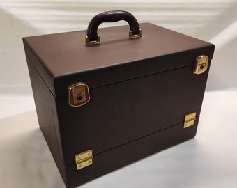 May include: A brown leather-bound box with a gold handle and gold clasps. The box has two compartments and is perfect for storing jewelry or other valuables.
