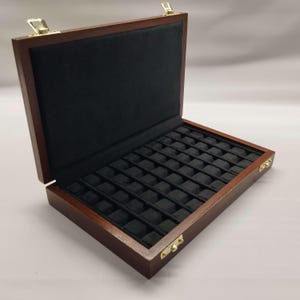 Puede incluir: Caja de joyería de madera abierta con acabado marrón oscuro, con interior de terciopelo negro y múltiples compartimentos pequeños. La caja tiene bisagras y un cierre de color latón, y está diseñada para guardar objetos pequeños.