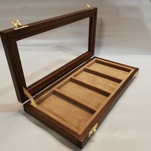 May include: A dark wood display case with a glass top and five compartments lined with brown felt. The case has brass hinges and clasps.