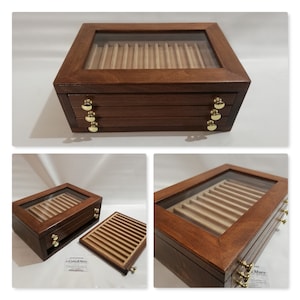 Könnte beinhalten: Eine Holzstiftebox mit Glasdeckel und drei Schubladen. Die Box ist aus dunklem Holz mit hellem Holzinnenraum. Die Schubladen haben Messingknöpfe.