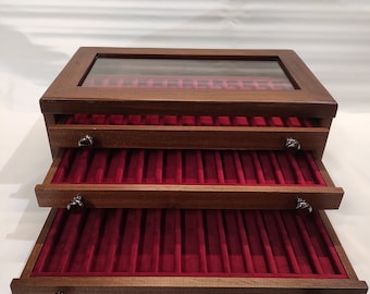 Könnte beinhalten: Eine Holzstiftebox mit drei Schubladen und einer Glasplatte. Die Schubladen sind mit rotem Samt ausgekleidet und haben schwarze Knöpfe. Die Box ist aus dunklem Holz.