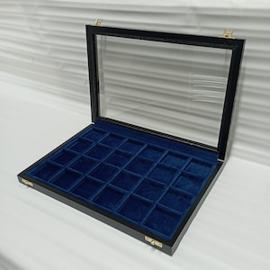 Peut inclure: Une vitrine en bois noir avec un dessus en verre et un revêtement en velours bleu. La vitrine comporte 24 compartiments pour ranger de petits objets.