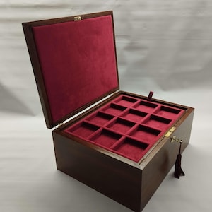 May include: A wooden jewelry box with a hinged lid, open to reveal a red velvet interior with multiple compartments. The box is rectangular, with a dark brown finish and a gold-colored clasp and key. A tassel hangs from the keyhole.