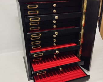 May include: A black wooden jewelry box with 10 drawers and a hinged door. The drawers have red felt lining and gold-colored labels. The box has a gold-colored handle on the bottom drawer.