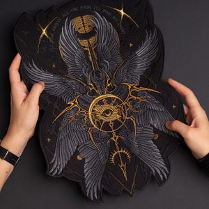 May include: A large black embroidered patch featuring a central golden eye surrounded by multiple grey wings. The design includes golden celestial motifs and the text "I'LL RISE ABOVE ALL THE PAIN, I'LL FIND MY LIGHT" arched across the top portion.