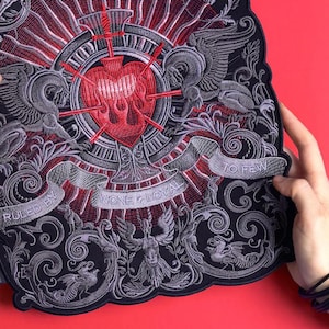 Könnte beinhalten: Gestickter Aufnäher mit einem von Schwertern durchbohrten Herzen, umgeben von Zierdetails und dem Text "NONE LOYAL TO FEW". Das Design weist rote, graue und schwarze Farben auf, mit einem detaillierten, strukturierten Aussehen. Der Aufnäher hat einen dekorativen, gotischen Stil.