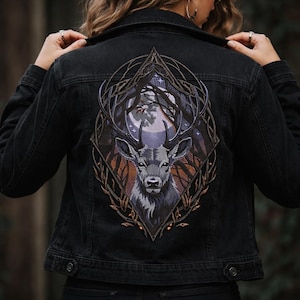 Puede incluir: Chaqueta vaquera negra con un parche bordado en la espalda. El parche muestra un ciervo con cuernos contra un bosque y un cielo iluminado por la luna. La chaqueta tiene un diseño clásico con cierre de botones y bolsillos.