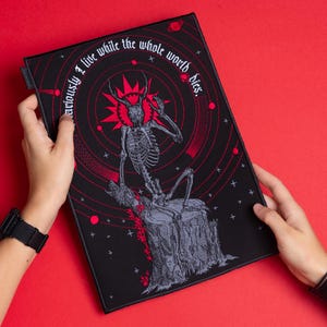 Peut inclure: Écusson rectangulaire noir avec une illustration rouge et grise d'un squelette avec des bois assis sur une souche d'arbre. Le patch porte le texte "I live curiously while the whole world dies." Le fond est noir avec des accents rouges.