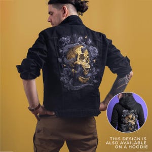 May include: Black denim jacket with a large embroidered design on the back featuring a gold skull, snakes, and roses. The jacket has long sleeves and a classic collar. The design is also available on a hoodie.
