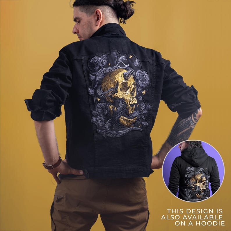 May include: Black denim jacket with a large embroidered design on the back featuring a gold skull, snakes, and roses. The jacket has long sleeves and a classic collar. The design is also available on a hoodie.