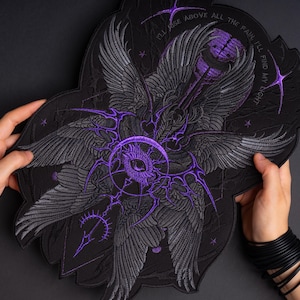 May include: A large black embroidered patch featuring a central purple eye surrounded by multiple grey wings and intricate purple linework. The text "I'LL RISE ABOVE ALL THE PAIN, I'LL FIND MY LIGHT" is stitched in purple along the top edge of the design.