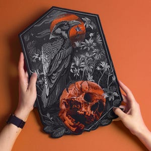 May include: A large, pentagonal embroidered patch featuring a detailed black raven perched above a weathered orange human skull. The design includes white floral elements and a circular orange sun background, all bordered by a thick black stitched edge.