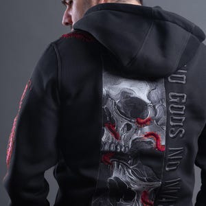 Könnte beinhalten: Ein schwarzer Kapuzenpullover mit einer großen Stickerei auf der Rückseite, die einen detaillierten Totenkopf mit roten Tausendfüßlern zeigt. Der Text NO GODS NO MASTERS ist vertikal in schwarzem Garn gestickt. Rote Tausendfüßler sind auch am Ärmel.