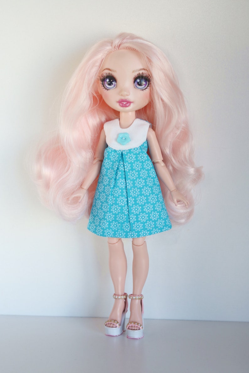 May include: A doll with pink hair wearing a blue and white floral dress and white shoes with pink accents.