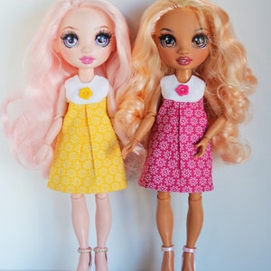 May include: Two dolls wearing floral print dresses. The doll on the left has pink hair and is wearing a yellow dress with white flowers. The doll on the right has brown hair and is wearing a pink dress with white flowers.