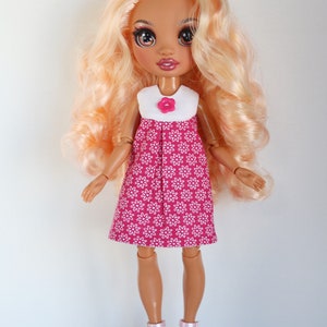 May include: A doll with long blonde hair wearing a pink dress with white flowers and pink shoes.