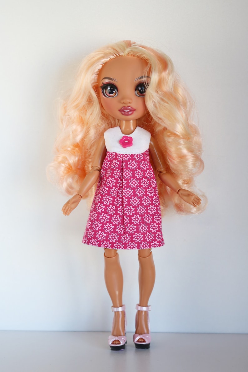 May include: A doll with long blonde hair wearing a pink dress with white flowers and pink shoes.