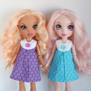 May include: Two dolls wearing dresses with floral patterns. The doll on the left has long, wavy, light blonde hair and is wearing a purple dress with white flowers. The doll on the right has long, wavy, pink hair and is wearing a turquoise dress with white flowers.