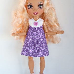May include: A doll with long blonde hair wearing a purple dress with white flowers and a white collar with a purple flower button. The doll is wearing pink high heels.