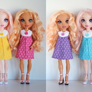 May include: Three dolls with long, flowing hair wearing different colored dresses with floral patterns. The dolls are wearing white collars with a single button on the front. The dolls are wearing white shoes with pink, yellow, and blue accents.