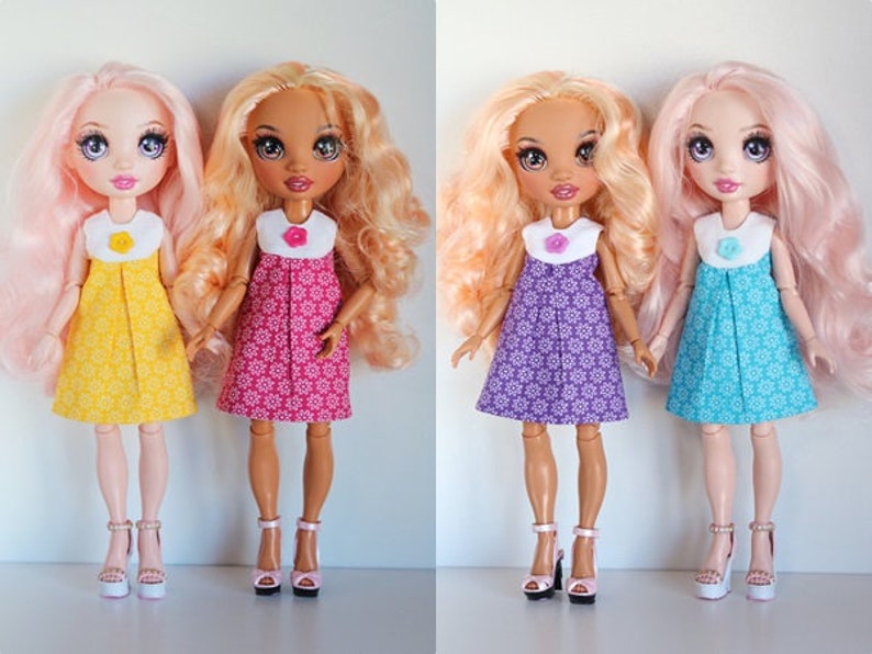 May include: Three dolls with long, flowing hair wearing different colored dresses with floral patterns. The dolls are wearing white collars with a single button on the front. The dolls are wearing white shoes with pink, yellow, and blue accents.