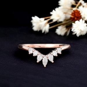 Puede incluir: Una fina banda de boda de oro rosa con un diseño curvo que presenta una fila de diamantes en forma de marquesa.