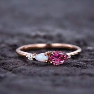May include: A rose gold ring featuring a pink pear-shaped gemstone, a white opal, and a small diamond.