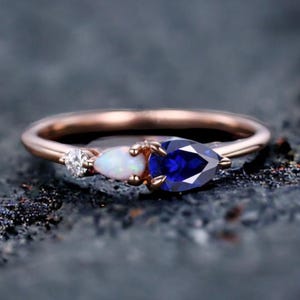 May include: A rose gold ring featuring a pear-shaped blue sapphire, a pear-shaped white opal, and a small round diamond.