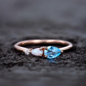 May include: A rose gold ring with a pear-shaped blue topaz gemstone, a pear-shaped opal gemstone, and a round diamond gemstone.