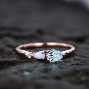 May include: A delicate rose gold ring with a pear-shaped aquamarine gemstone, a smaller round diamond, and a pear-shaped opal.