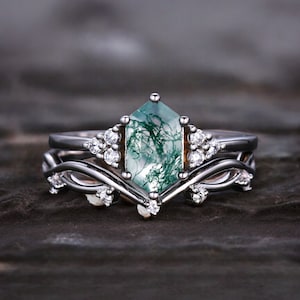 Op de afbeelding: Een zwarte en witte ringset met een groene mosagaat edelsteen. De middelste steen is zeshoekig en is omgeven door kleinere witte edelstenen. De band is een delicaat, gedraaid ontwerp.