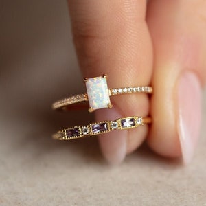 May include: A gold ring set with a white opal gemstone and a smaller band of gold with small white gemstones. The ring is worn on a finger.