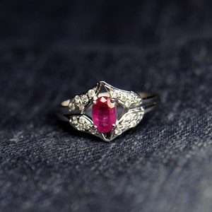 Puede incluir: Un anillo de plata con una piedra preciosa ovalada de rub&iacute; rojo rodeada de peque&ntilde;as piedras blancas.