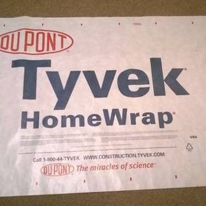 May include: A white roll of Tyvek HomeWrap building wrap with the DuPont logo and the text "Call 1-800-44-TYVEK WWW.CONSTRUCTION.TYVEK.COM  OU PONT The miracles of science"