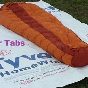May include: An orange and red sleeping bag with the words "Anchor Tabs" printed on a white background.