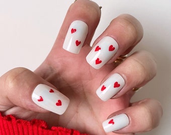May include: White nail polish with red heart designs on each finger.