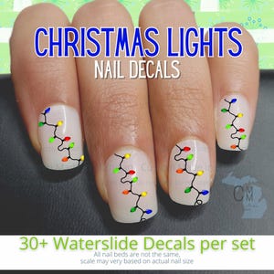 May include: A set of 30+ waterslide nail decals featuring a string of Christmas lights with red, green, yellow, and blue bulbs. The decals are shown on a set of fingernails.