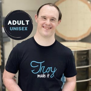 May include: A black t-shirt with a blue and white design that says "Troy made it". The shirt is unisex and for adults.