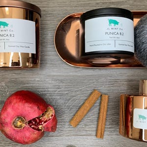 May include: A set of home fragrance products in a copper finish. The set includes a candle, a reed diffuser, and a small decorative object. The candle and diffuser both have the text "PUNICIA 8.2" on the label. The decorative object is a small, round, gray object.