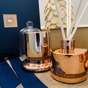 Puede incluir: Un conjunto de dos productos de fragancia para el hogar con aroma a rosa y bergamota. Una vela dorada con tapa de vidrio y un difusor dorado con ca&ntilde;as blancas. Ambos productos tienen una etiqueta que dice "Rose & Bergamota".