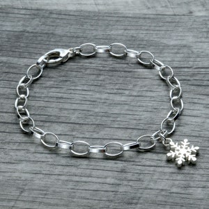 May include: A silver chain bracelet with a snowflake charm. The bracelet is made of oval links and has a lobster clasp.
